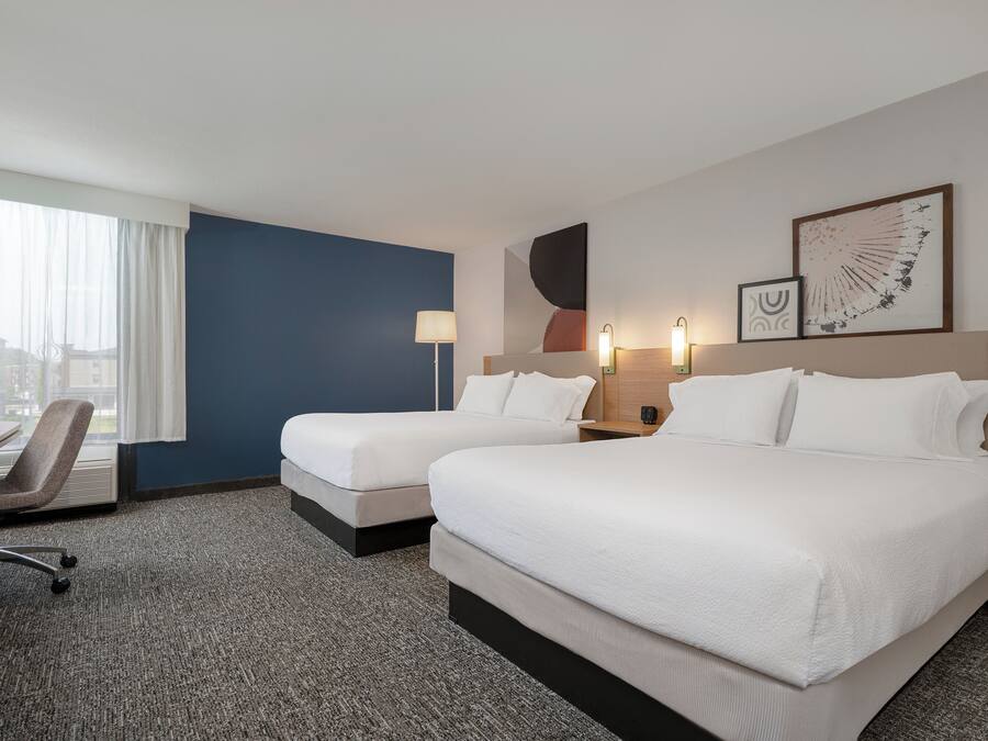 Ein Hotelzimmer mit zwei Betten, einem Schreibtisch, einem Stuhl und einem großen Fenster mit Vorhängen.