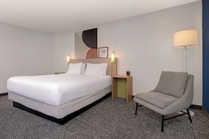 A hotel room with a bed, a chair, a nightstand, a wall art piece, and a lamp.