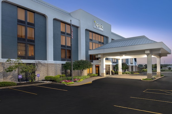 Hotel com fachada moderna, entrada coberta e estacionamento.