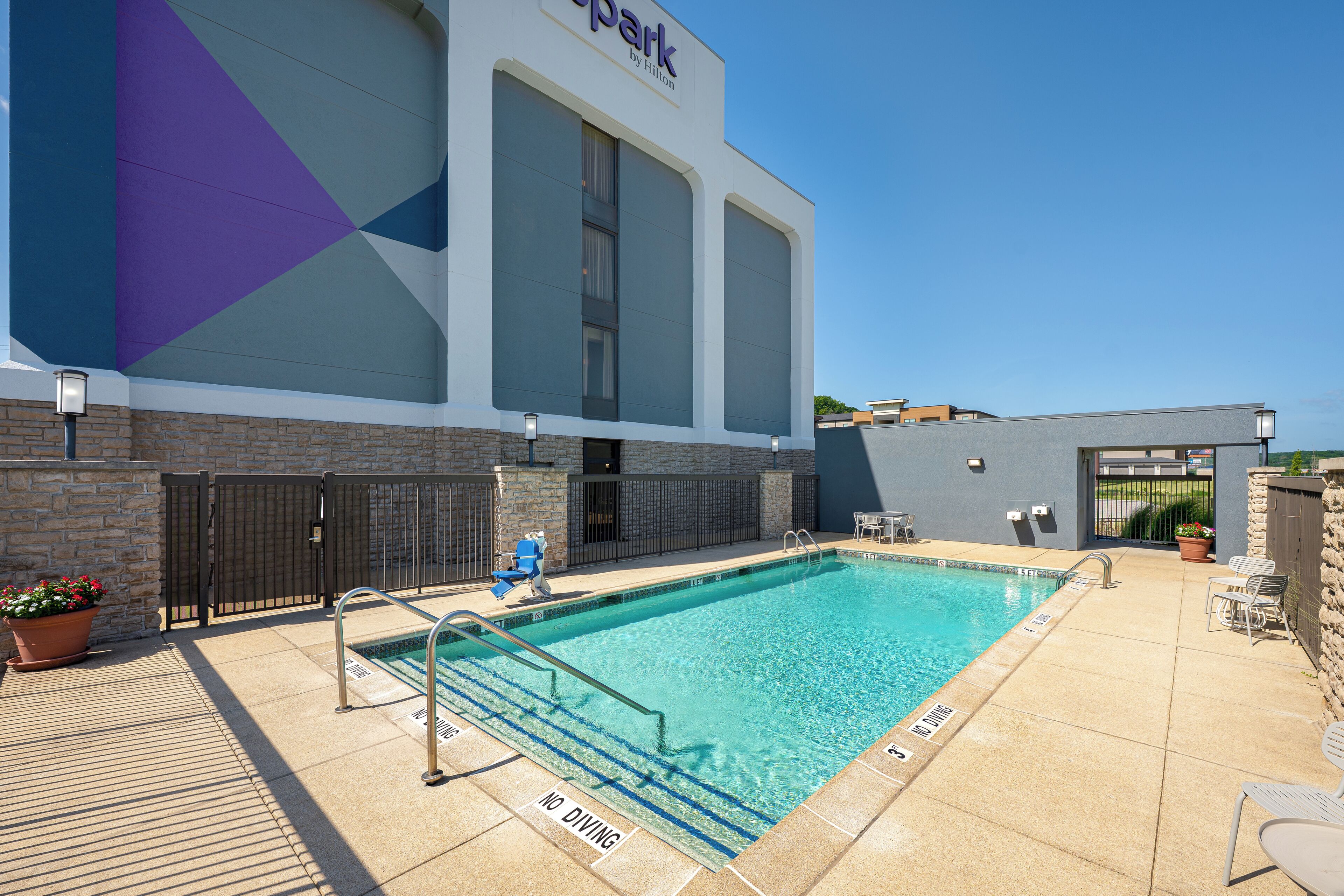 A hotel with a swimming pool, outdoor seating, and a clear sky.