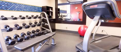 A gym with a treadmill, dumbbells, and a mirror.