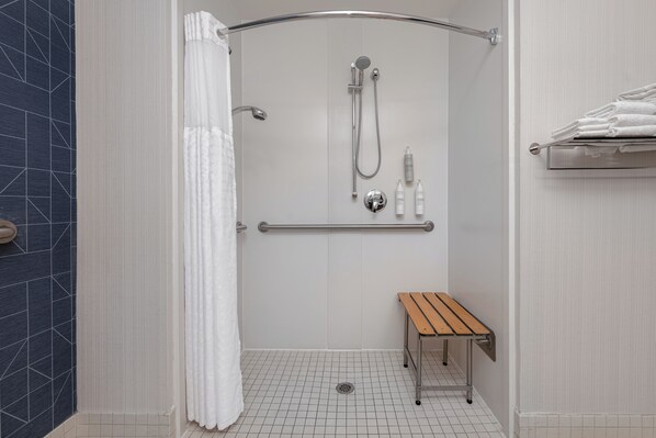 A shower area with a handheld showerhead, a handheld shower attachment, a grab bar, and a small wooden bench.