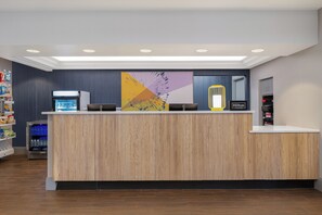 A hotel reception desk with a wooden finish, a digital screen, and a vending machine. - Spark by Hilton St. Louis Southwest (Valley Park)