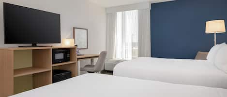 Quarto de hotel com duas camas, escrivaninha com televisão de tela plana, micro-ondas, cadeira e janela com cortinas.
