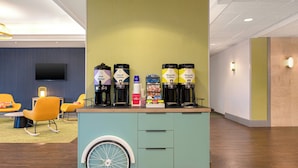 A coffee station with two types of coffee dispensers, a television, and seating with a modern design.