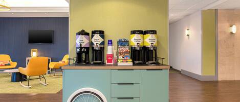 A coffee station with two types of coffee dispensers, a television, and seating with a modern design.