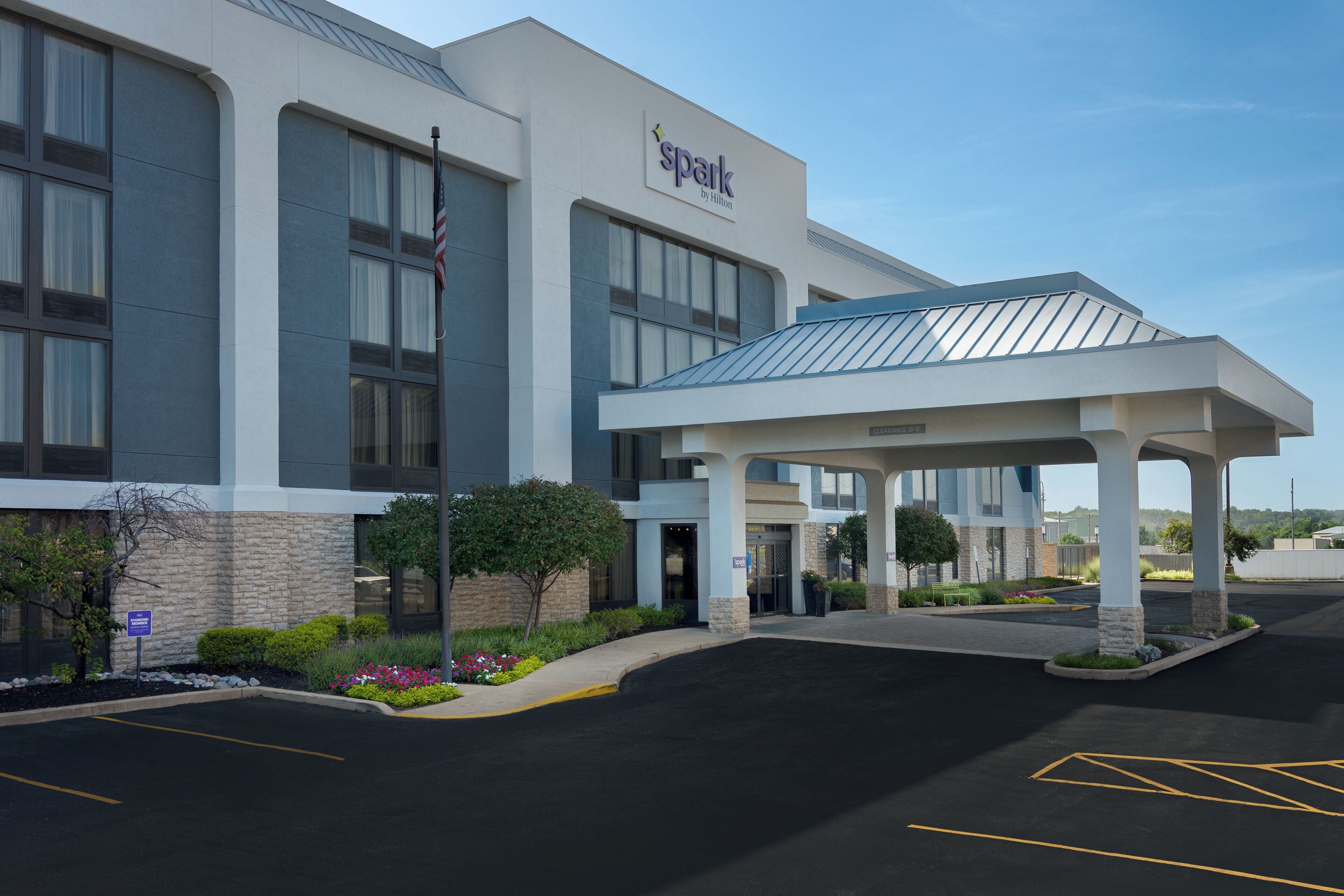 A hotel with a covered entrance, a flag, and a parking lot.