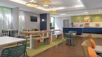 A modern dining area with wooden tables and chairs, a kitchen with blue cabinets, and a green accent wall.