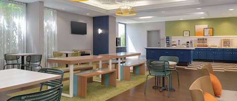 A modern dining area with wooden tables and chairs, a kitchen with blue cabinets, and a green accent wall.