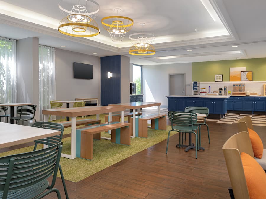 A modern dining area with wooden tables and chairs, a kitchen with blue cabinets, and a green accent wall.