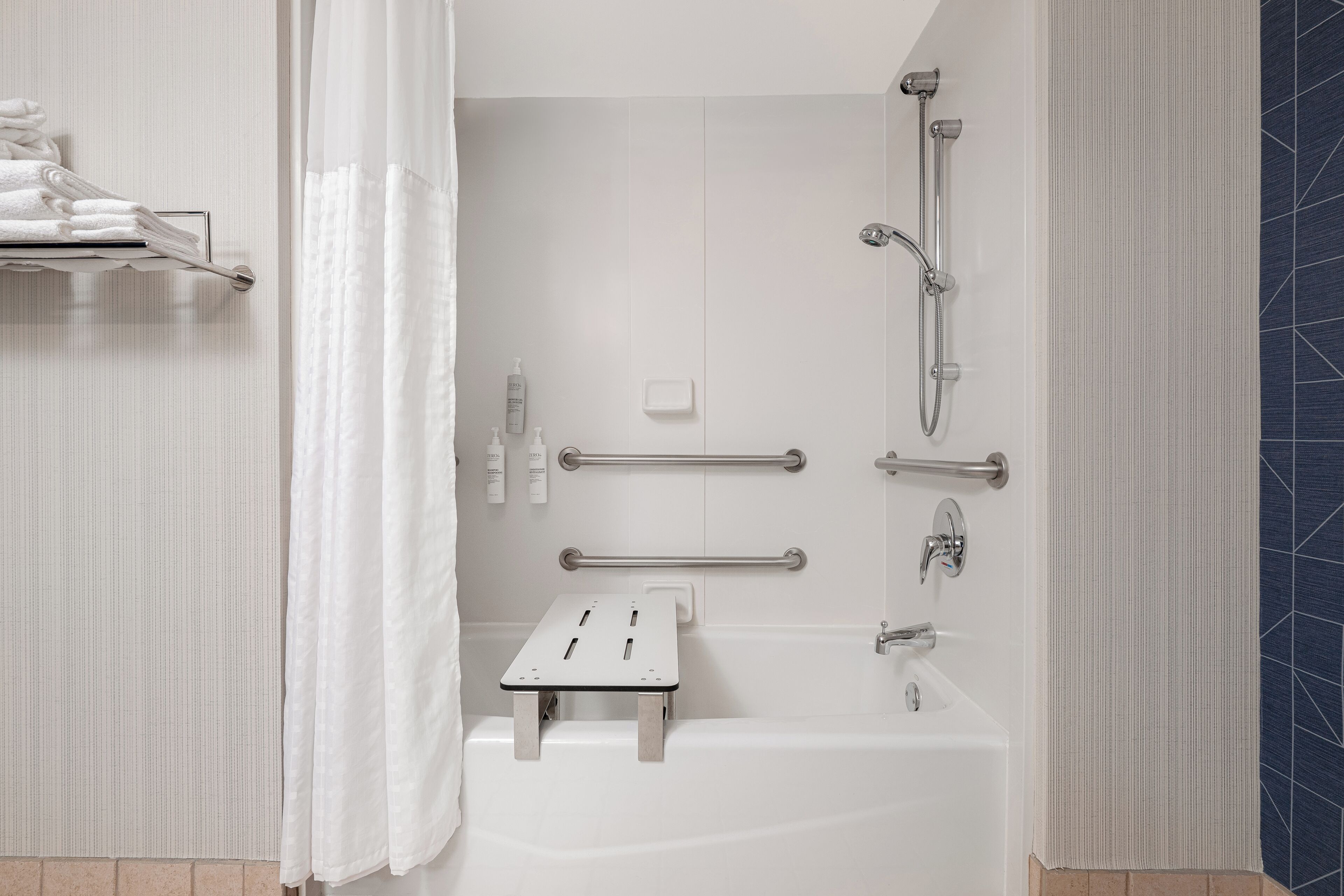 A modern bathroom with a bathtub, shower, and handrails.