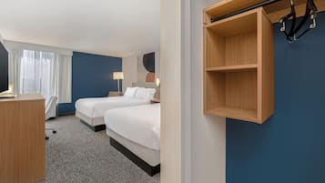 Ein Hotelzimmer mit zwei Betten, einem Schreibtisch, einem Stuhl, einem Kleiderständer und einem Wandregal.