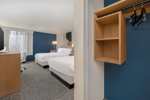 Habitació d'hotel amb dos llits, una taula de treball, una cadira, un penjador i una estantanya fixada a la paret.