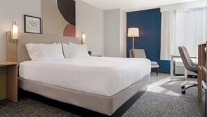 Et hotelværelse med en stor seng, et skrivebord, en stol og en lampe.