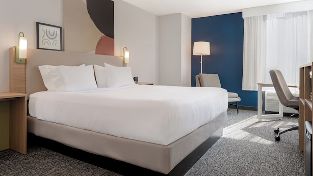 A hotel room with a large bed, a desk, a chair, and a lamp.