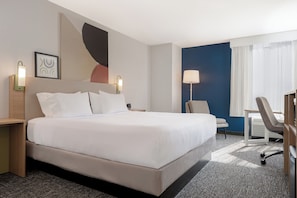 Quarto de hotel com uma cama grande, uma mesa, uma cadeira e uma luminária.