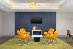 A room with a flat-screen TV mounted on the wall, two rocking chairs, a small table, and a yellow pendant light.