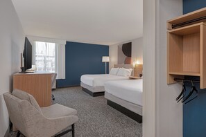 Habitación de hotel con dos camas, un escritorio, una silla, un televisor y una ventana con cortinas.