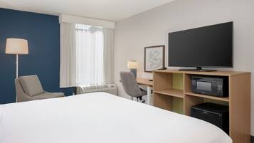 A hotel room with a bed, a desk, a chair, a television, a microwave, and a window with curtains.