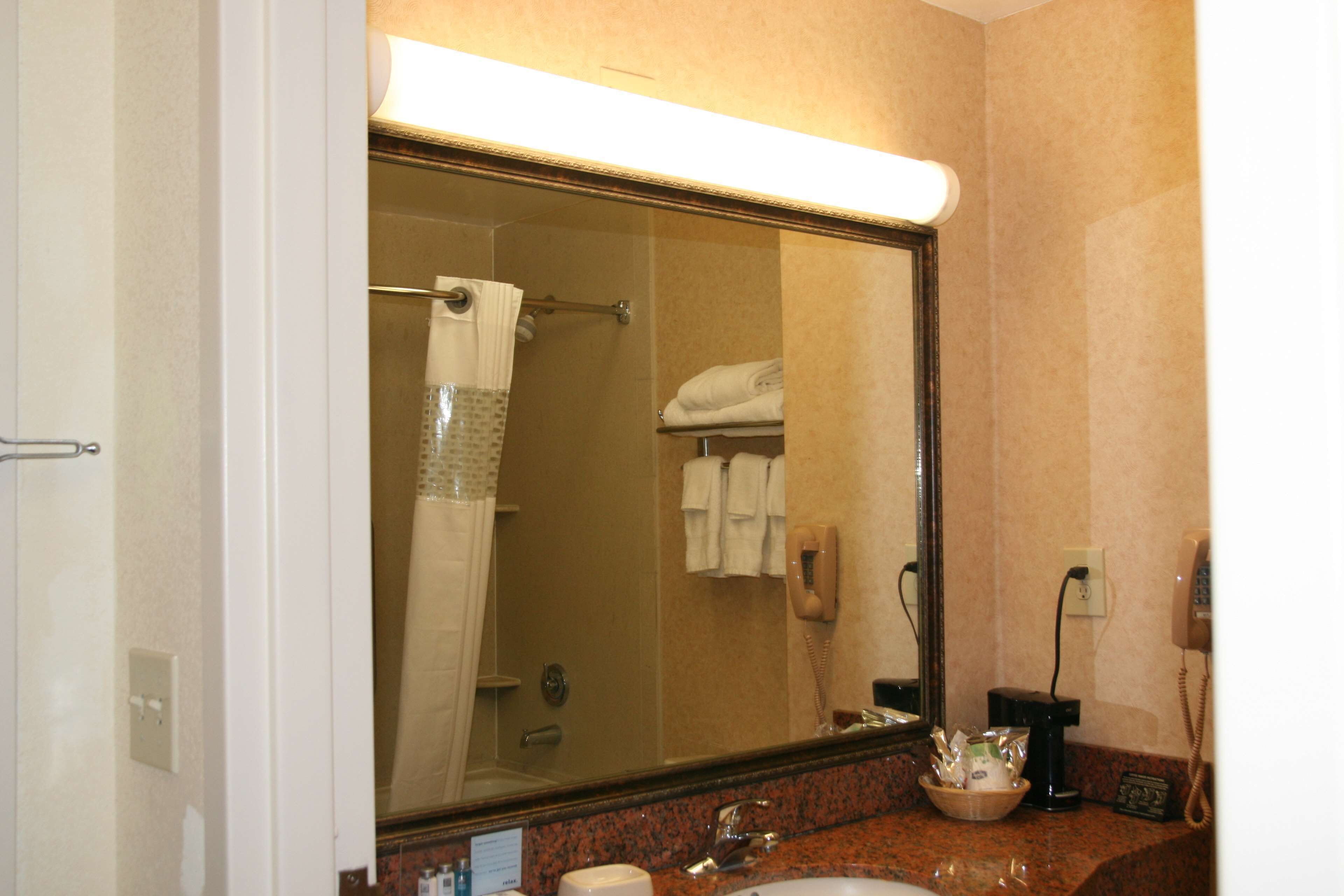A hotel bathroom with a large mirror, a sink, a towel rack, and a telephone.