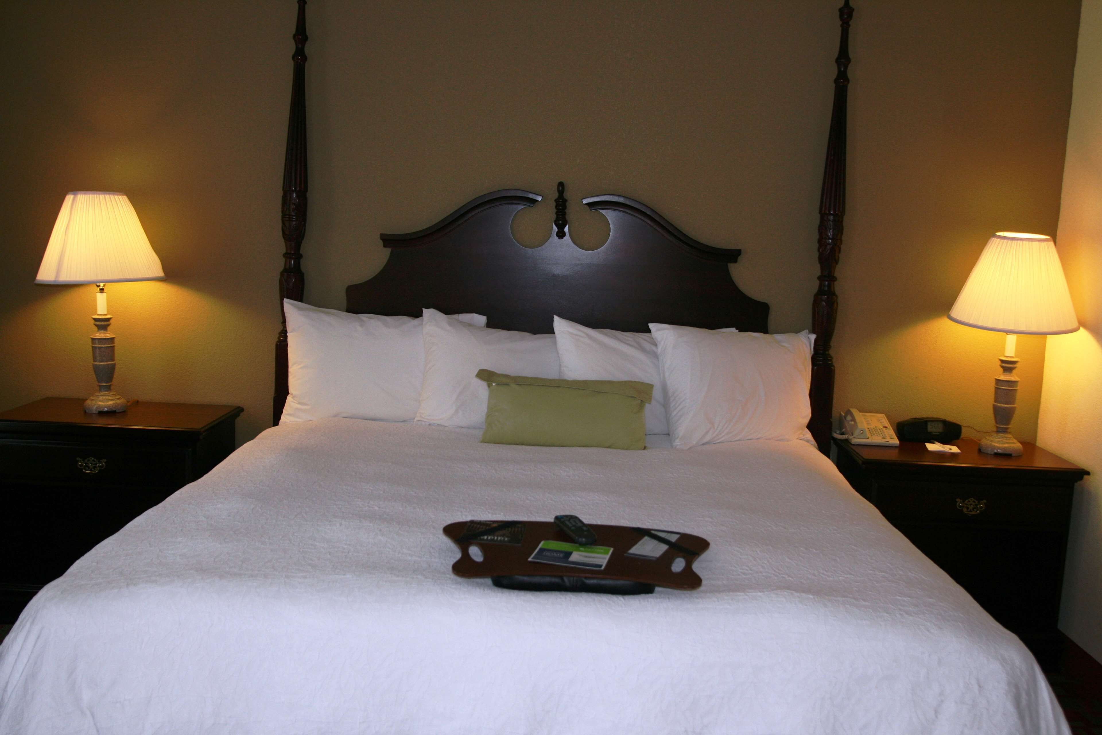 Cama arrumada com bandeja de produtos de higiene, duas luminárias de mesa e cabeceira de madeira.