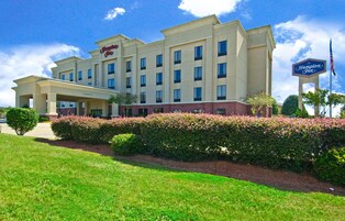 A Hampton Inn hotel with a clear sky, well-maintained lawn, and a signboard.