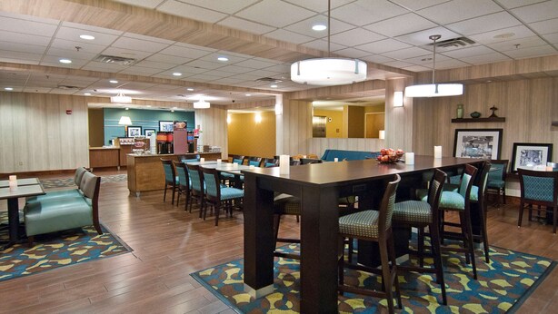 A hotel lobby with a large dining table, multiple chairs, a reception desk, and a patterned carpet. - Hampton Inn Canton (Canton)