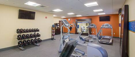 A gym with treadmills, elliptical machines, and a rack of dumbbells.