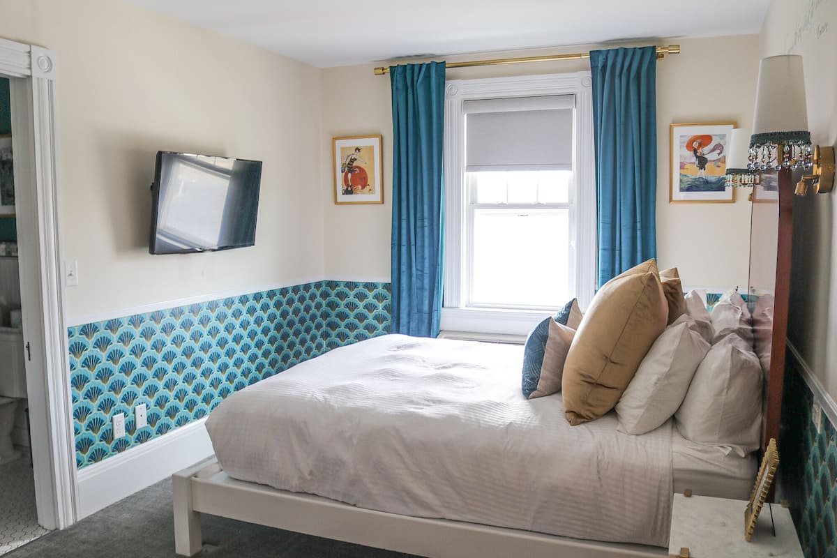 A bedroom with a bed, a television mounted on the wall, and a window with blue curtains.
