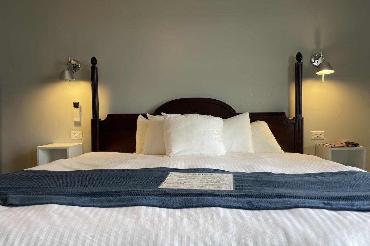 A neatly made bed with white and blue bedding, two bedside tables with lamps, and a wall-mounted thermostat.