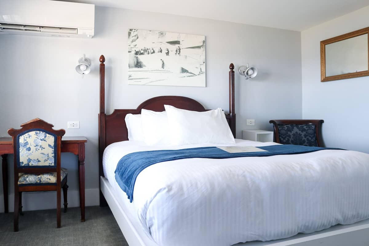 A neatly made bed with white and blue bedding, a wooden headboard, and a bedside table with a lamp.