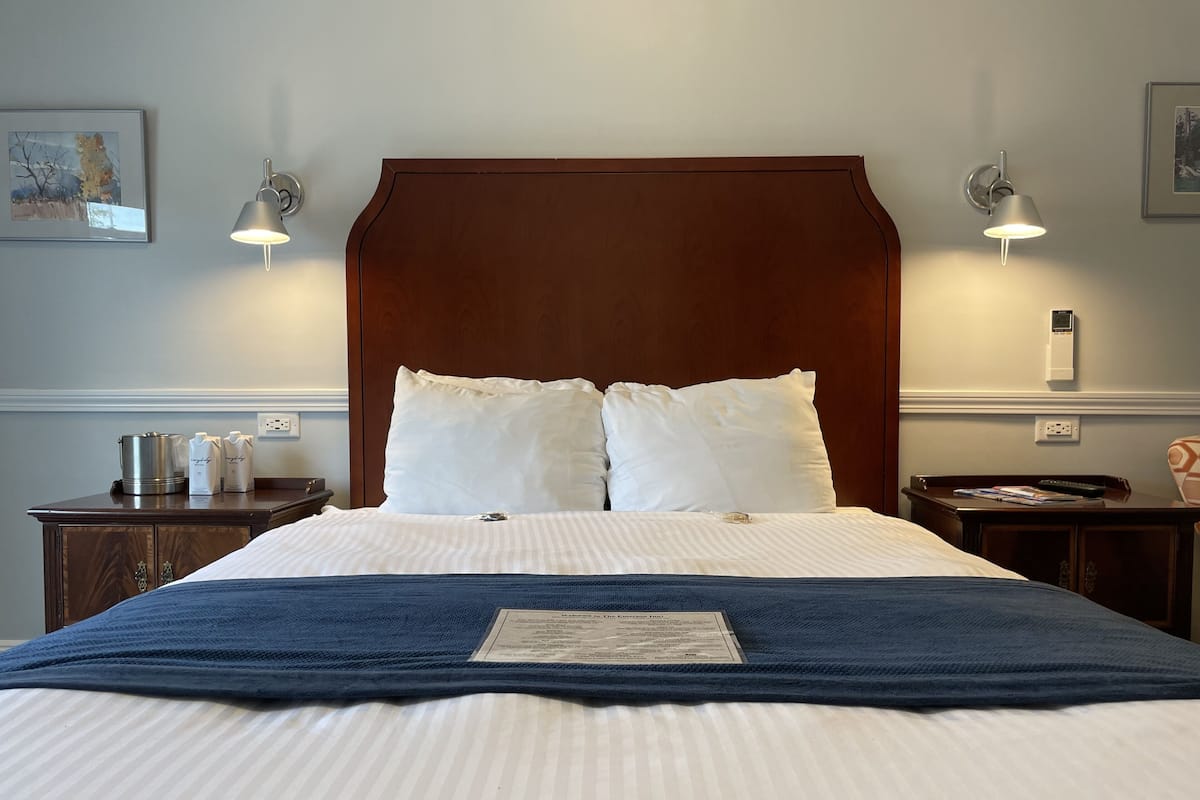 A neatly made double bed with a wooden headboard, two bedside tables with lamps, and a framed picture on the wall.