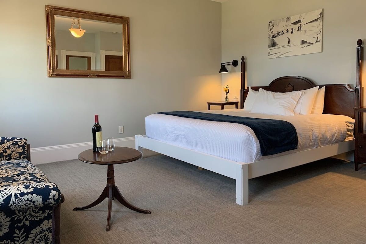 A bedroom with a bed, bedside table, lamp, and a chair.