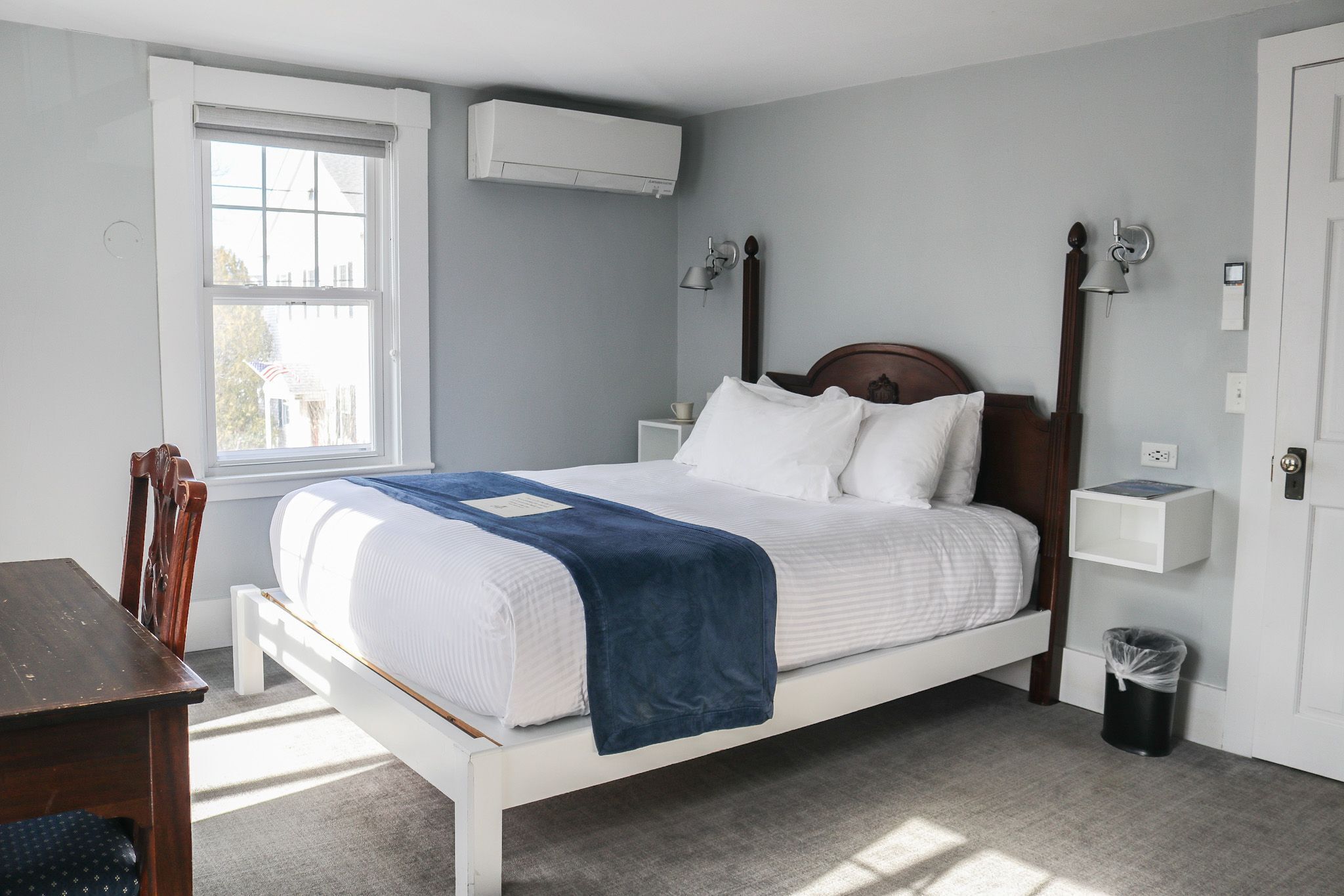 Un lit bien fait, avec une couverture bleue, une tête de lit en bois et deux lampes de chevet.