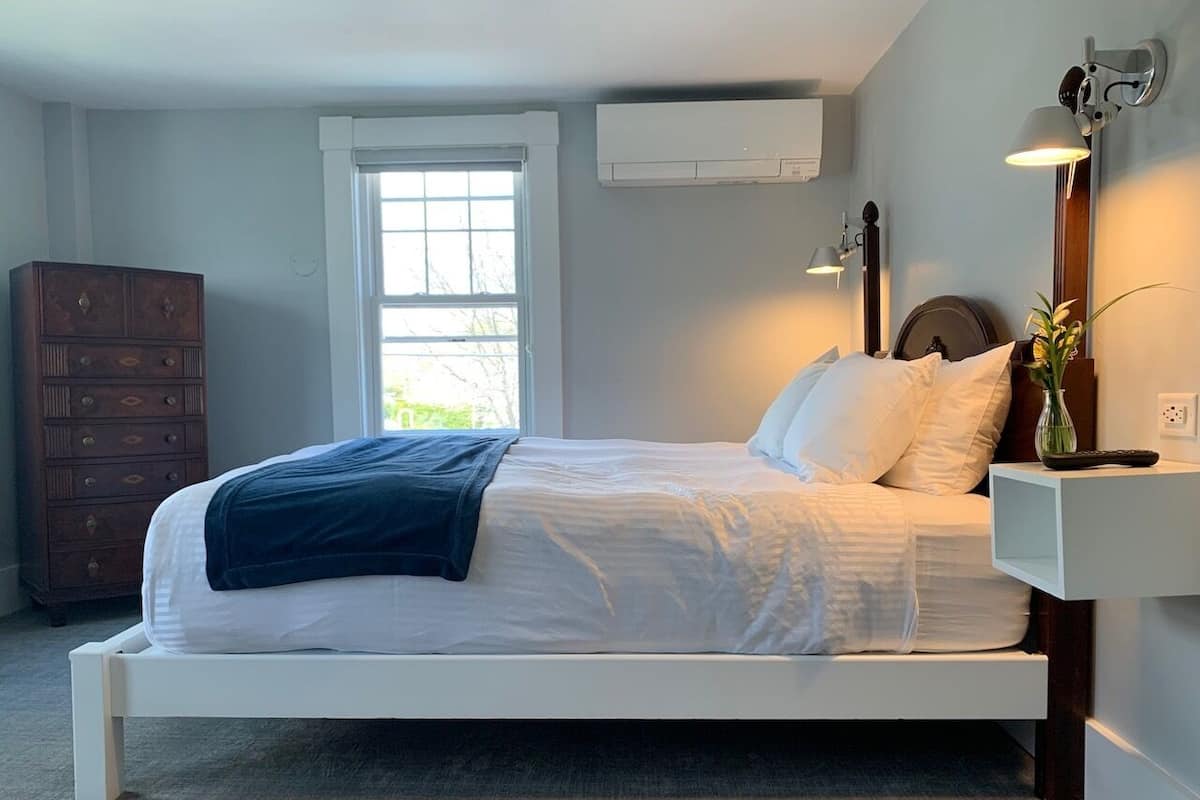 A modern bedroom with a white bed, a dresser, a window, and a wall-mounted lamp.