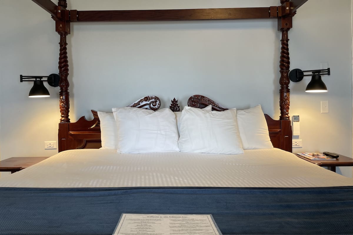 A four-poster bed with a dark wooden frame and a white bedspread. There are two wall-mounted lamps on either side of the bed.
