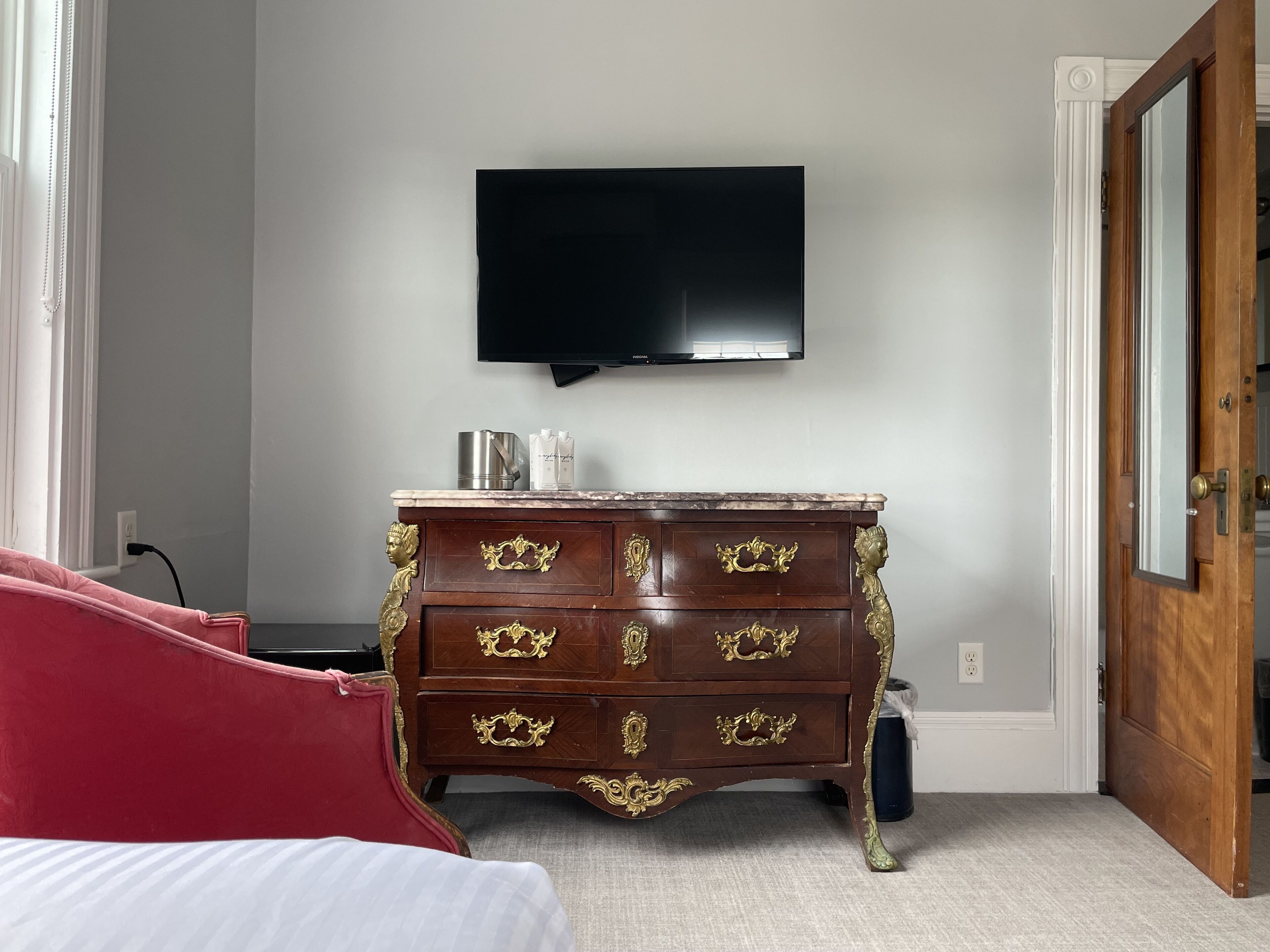 Una camera da letto con un comò in legno, una televisione montata a muro e una sedia rossa.