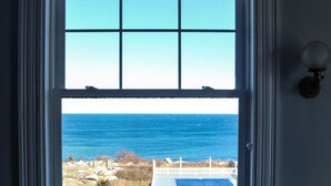 A room with a large window overlooking the ocean, two patterned armchairs, and a small table with a book. - Emerson Inn (Rockport)
