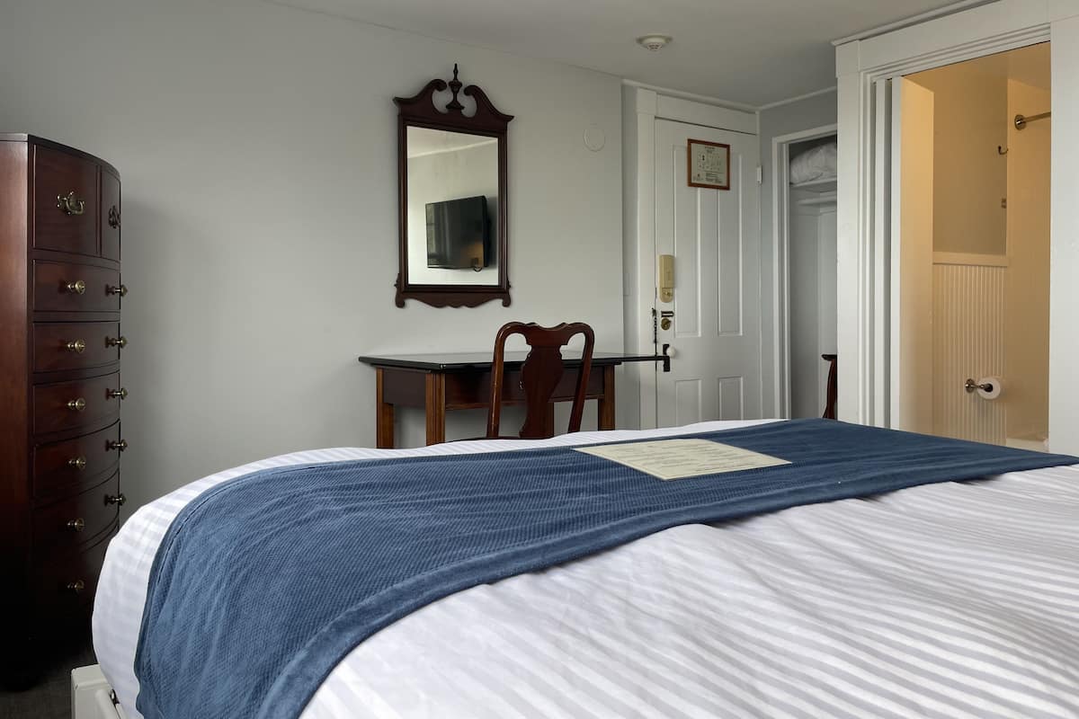 A bedroom with a bed, dresser, desk, chair, and a door leading to another room.