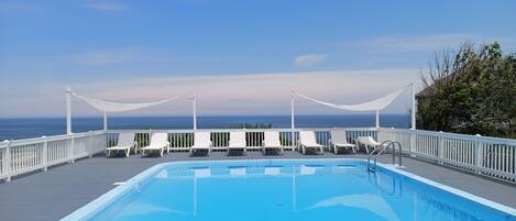 En pool med vita solstolar och utsikt över havet.