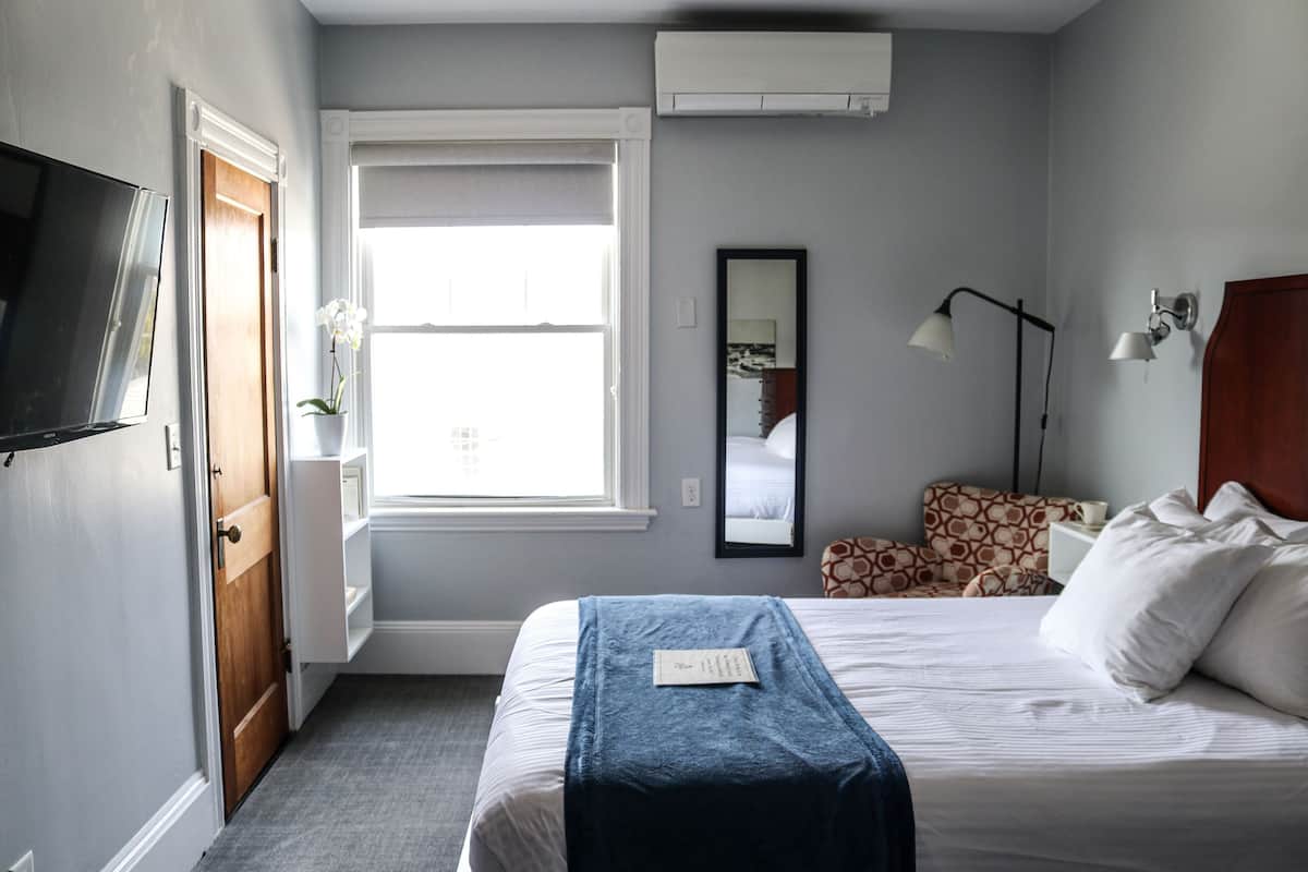 A bedroom with a bed, a TV, a window, a mirror, and a bedside lamp.