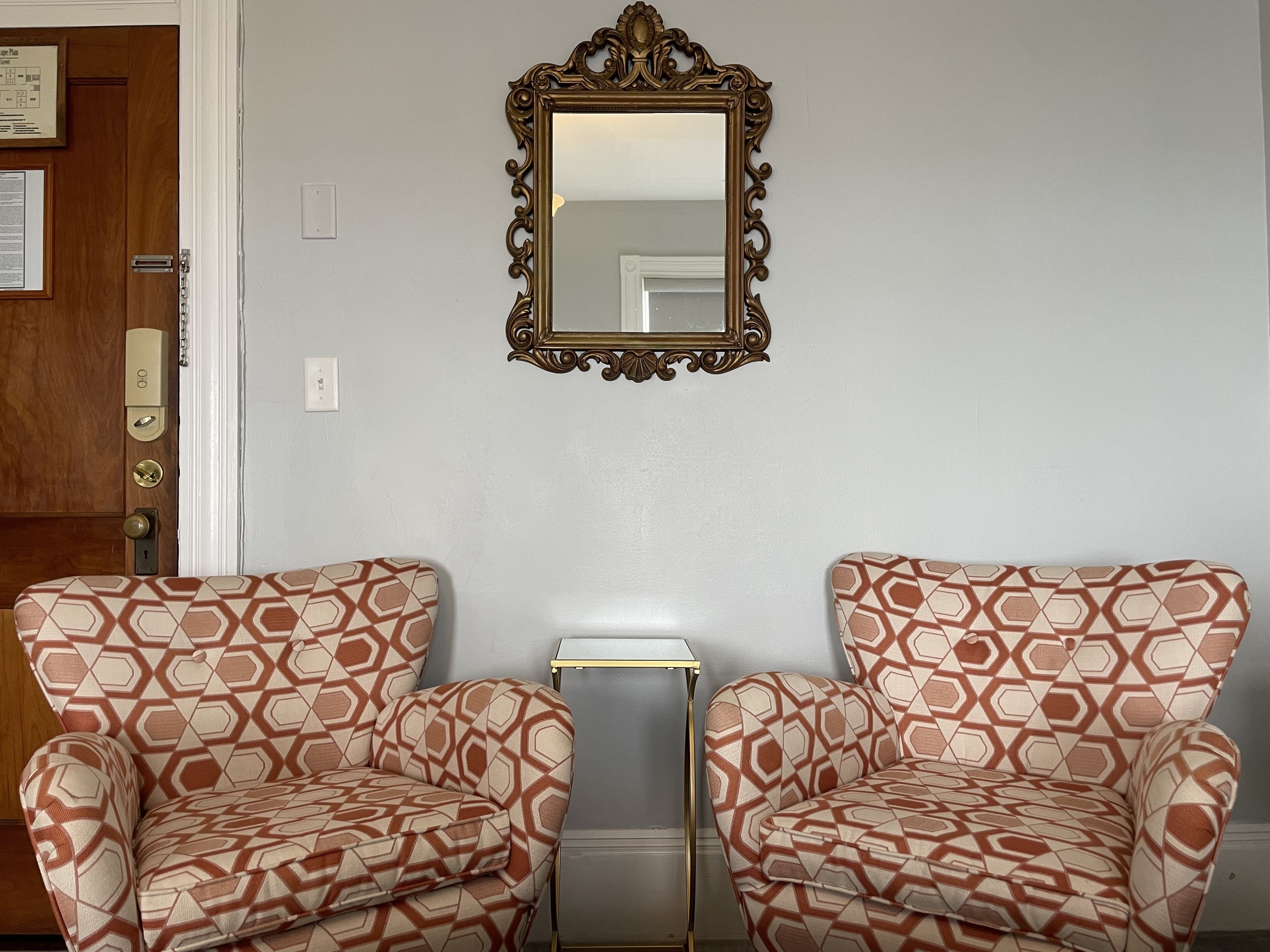 Two patterned armchairs, a small table, and a mirror on a plain wall.