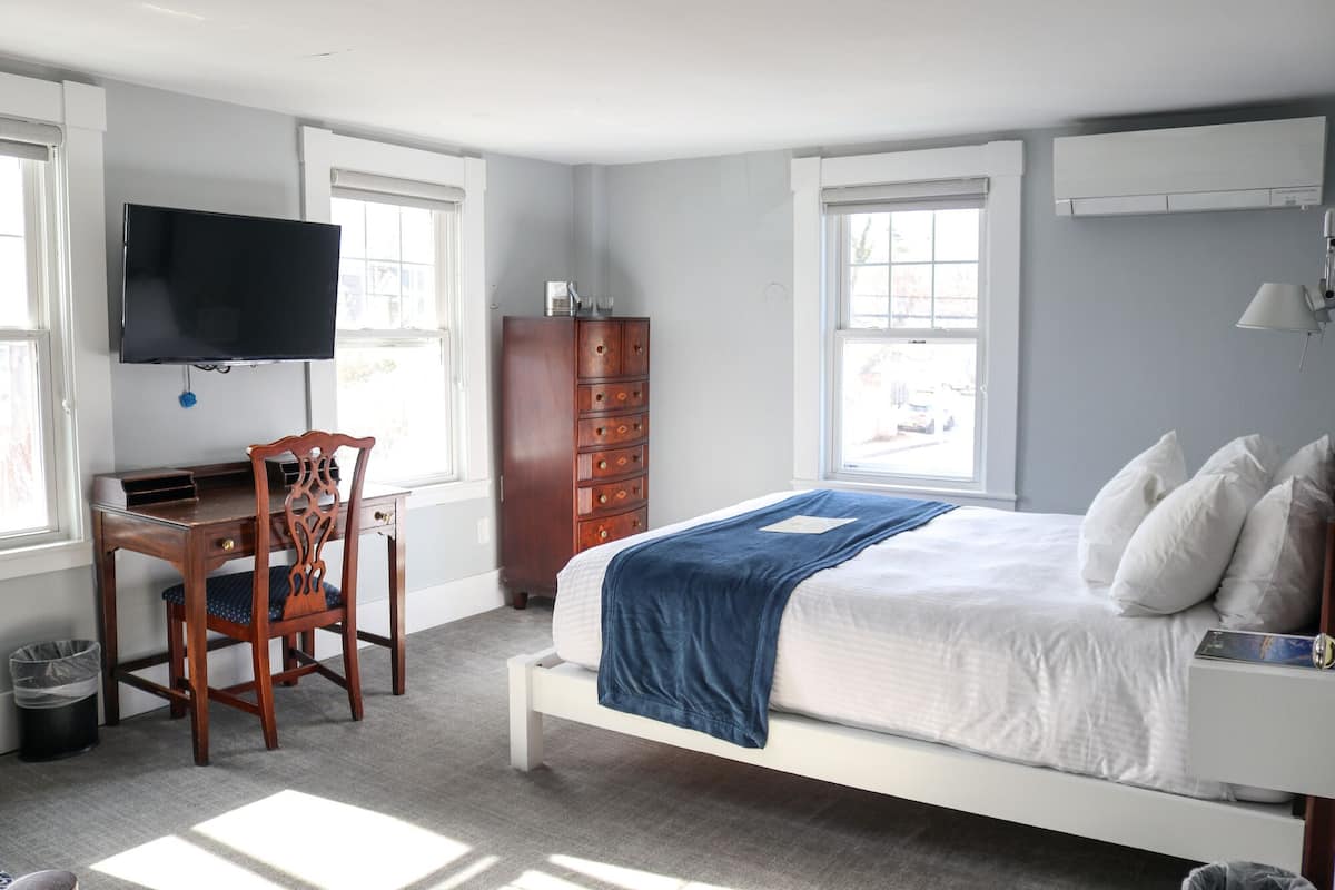 A bedroom with a bed, a desk, a chair, a TV, a wardrobe, and a window.
