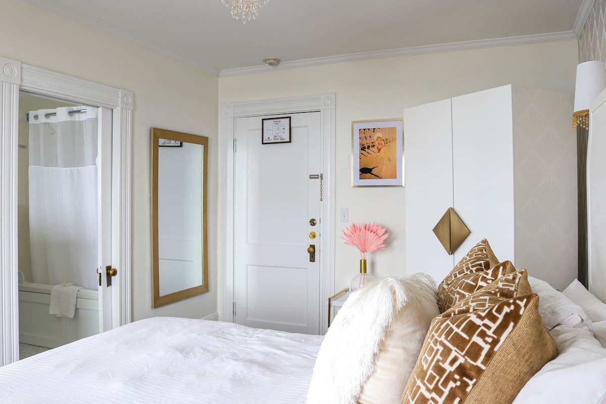 A bedroom with a large bed, a mirror, a door, and a framed picture on the wall.