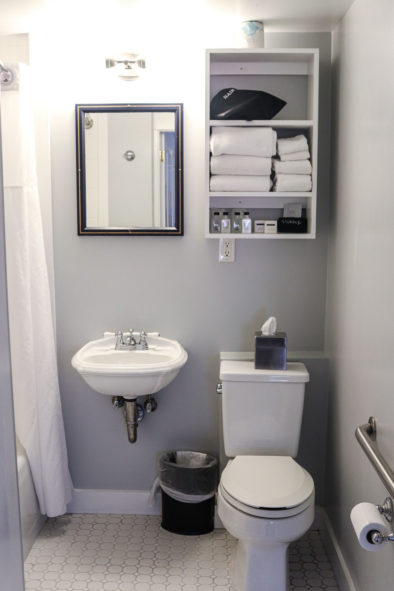 Une salle de bain équipée d’un lavabo, de toilettes et d’une étagère au-dessus des toilettes pour y ranger les articles de toilette.