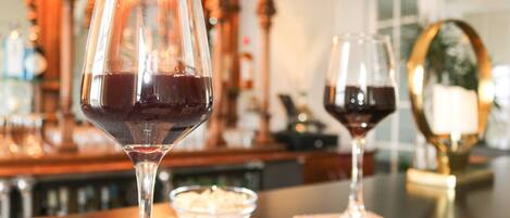 Two wine glasses on a bar counter with a candle and a bowl of snacks in the background.