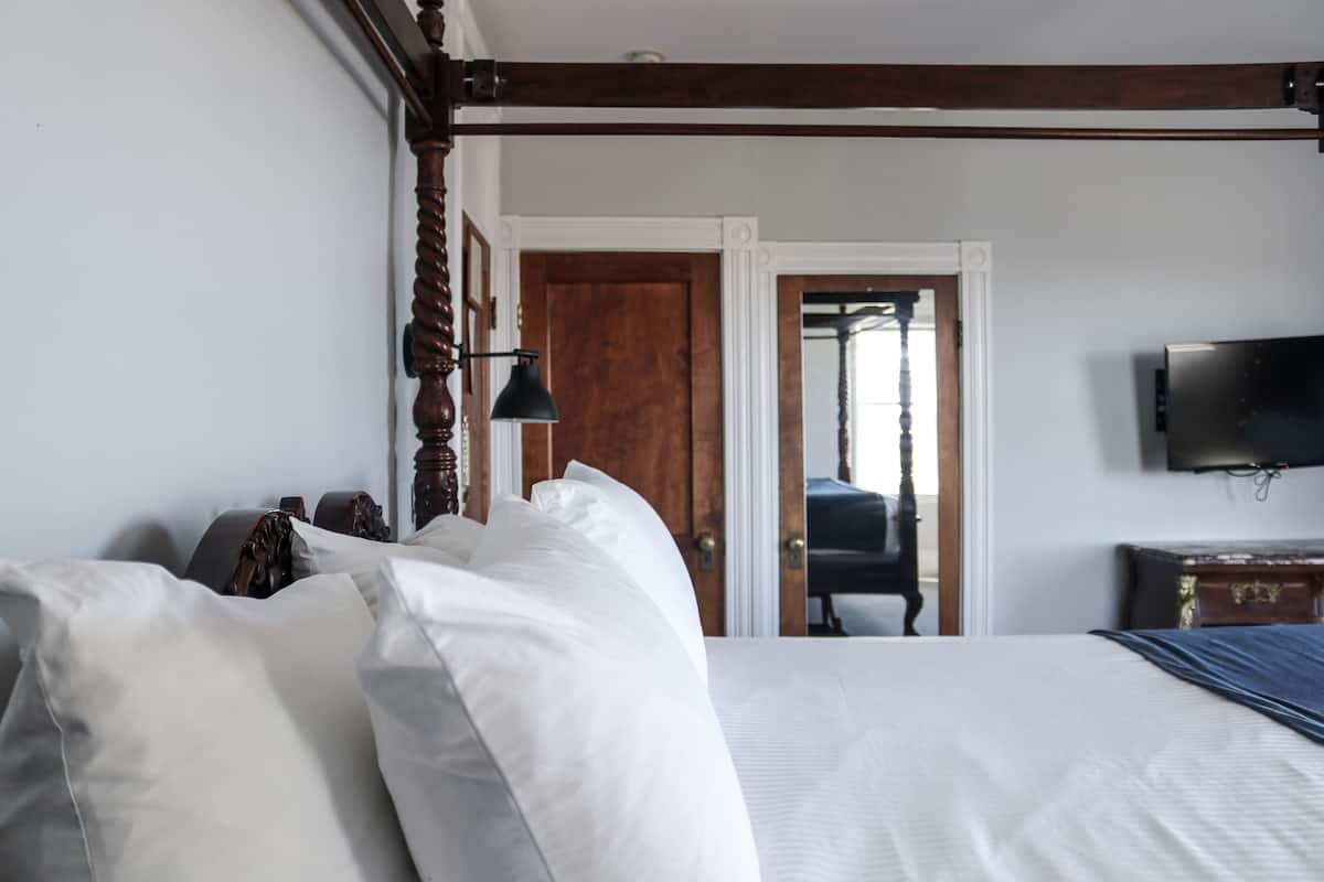 A hotel room with a large bed, a wooden headboard, a flat-screen TV mounted on the wall, and a door leading to another room.