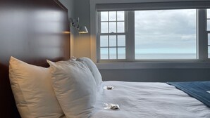 A hotel room with a large window, a bed with white linens, and a wooden headboard. - Emerson Inn (Rockport)