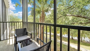 A balcony with wicker chairs, a glass table, and a view of trees and a pathway. - Bahama Bay Resort (Davenport)
