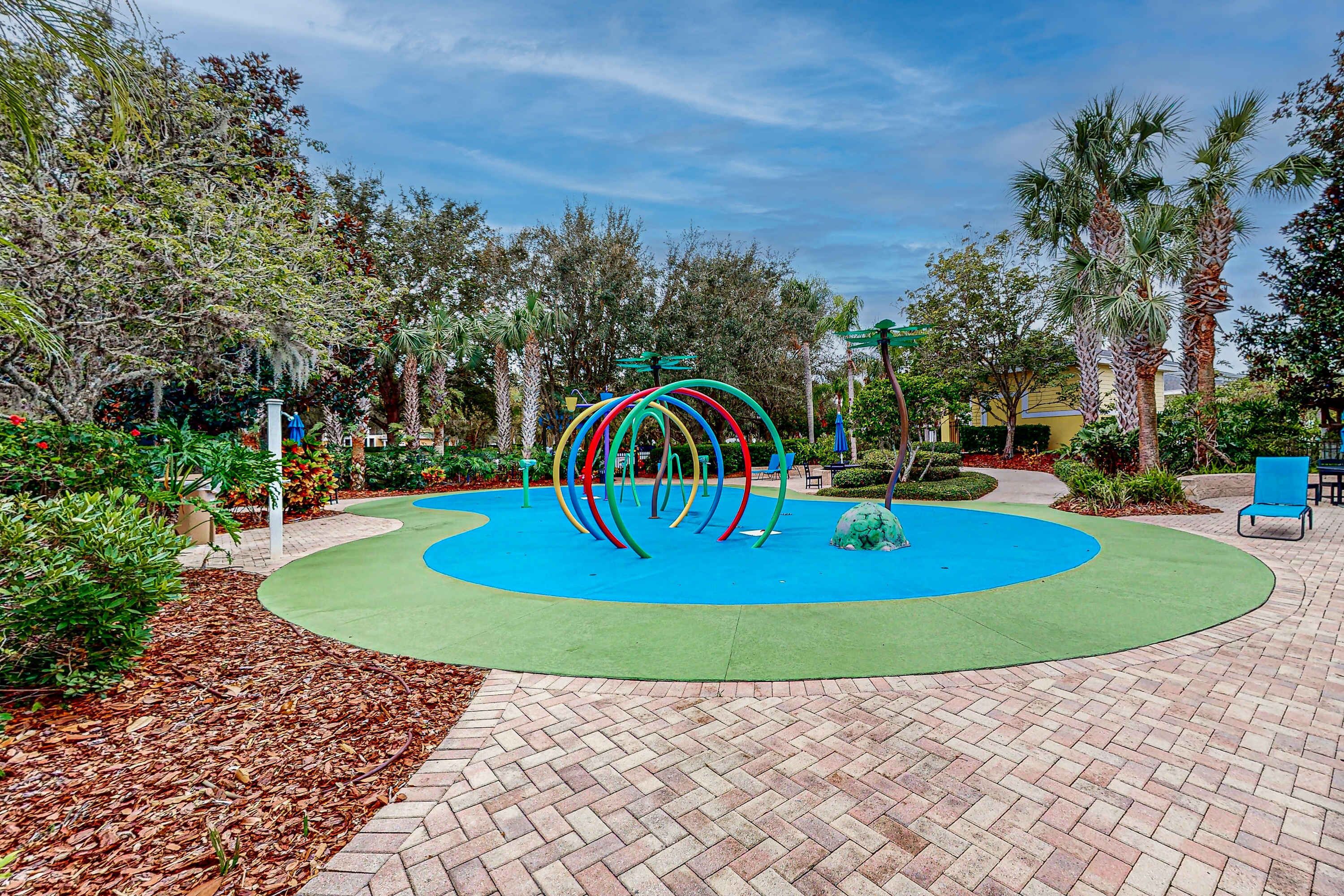 A landscaped area with a circular play zone, a brick pathway, and surrounding greenery.